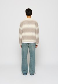 Beige and cream striped oversized sweater with a ribbed hem, paired with light blue wide-leg jeans. Smooth texture, casual design.