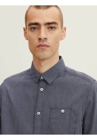 Camisa de botones de fondo azul marino con estampado, cuello y bolsillo, con botones blancos, hecha de un tejido ligero.