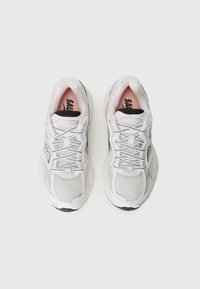 Baskets de sport gris clair avec un upper en mesh, présentant des accents blancs, un logo noir et un col rembourré. Les lacets sont fins et réfléchissants.