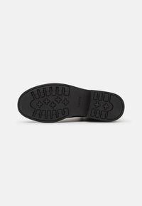 Suela de zapato de goma negra que presenta un patrón de relieve con formas rectangulares y cruzadas. Nombre de la marca "Levis" estampado en el lateral. Textura suave.