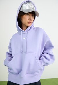 Sweatshirt roxo com capuz, bolso frontal e cordões, apresentando um pequeno logótipo branco da Nike no peito. Tecido suave, corte descontraído.