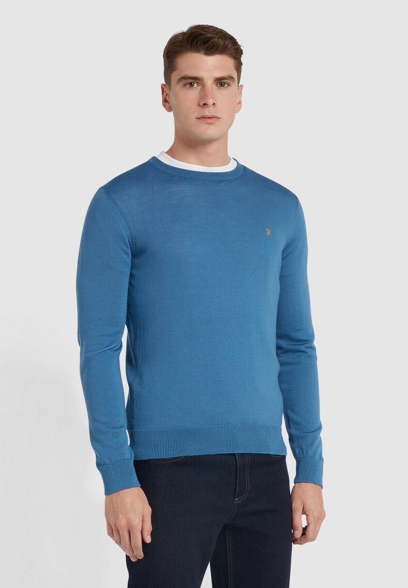 Niebieski sweter robiony na drutach z okrągłym dekoltem oraz ściągaczami na mankietach i dolnej krawędzi. Zawiera mały detal z logo na klatce piersiowej. Gładka tekstura, średnia waga.