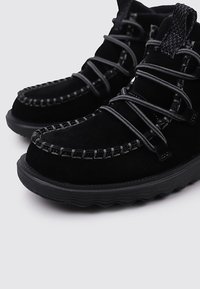 Botas de tobillo de ante negro con un acabado texturizado, que presentan costuras en contraste, una suela flexible y un sistema de cordones resistente.
