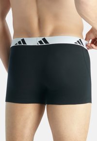 Svarta boxershorts med en tät passform och ett vitt midjeband med svarta Adidas-logotyper; mjukt tyg med en minimalistisk design.