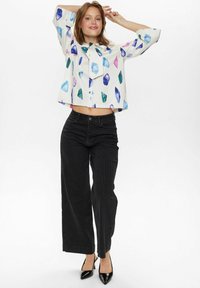 Top bianco corto con motivi geometrici di cristalli multicolori; abbinato a pantaloni neri a righe con gamba larga e tacchi a punta neri.