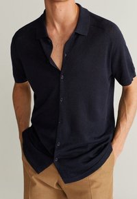 Camicia blu navy a maniche corte con bottoni, realizzata in tessuto testurizzato, dotata di collo e orlo leggermente curvo.