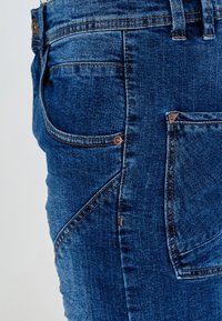 Blugi din denim albastru închis, cu croială ajustată, multiple buzunare, cusături contrastante și un patch cu brand pe buzunarul din spate.