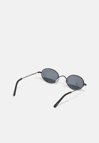Black oval sunglasses with dark lenses, thin metal frame, silicone nose pads, and slender black arms. Minimalist design with no visible accents.