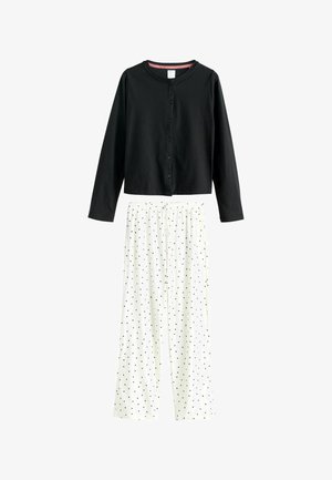 Schwarzes Langarmhemd mit Knopfverschluss, kombiniert mit weißen weiten Hosen mit schwarzem Punktenmuster, auf weißem Hintergrund präsentiert.