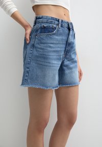 Vaatekappaleet: vaaleansiniset farkkushortsit, joiden alaosa on lörpöttävä. Viisi taskua, nappisulkeminen ja hienovarainen kuluminen edessä.