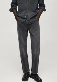 Jeans in denim grigio scuro con taglio dritto e cuciture visibili. Abbinati a una camicia a maniche lunghe slim-fit di colore scuro e calzature nere.