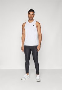 Hvid herretanktop uden ærmer med sort logo, parret med sorte tætsiddende leggings og hvide sportssko. Glat stof og slankt design.
