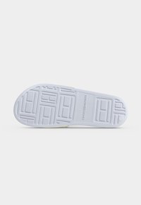 Semelle d'une basket blanche avec motif géométrique texturé antidérapant et logo "Tommy Hilfiger" embossé sur la zone de la voûte plantaire.