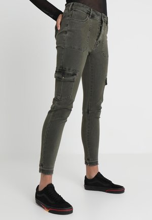 Olijf groene cargobroek in denimmix, met meerdere zakken, een slanke pasvorm en een rafelige rand. Gecombineerd met zwarte sneakers met rode accenten.