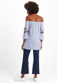 Sininen ja valkoinen raidallinen olkaimeton paita, jossa on kukkakirjontaa kellohelmoissa. Yhdistetty tummansinisiin leveälahkeisiin farkkuihin ja valkoisiin tennareihin.