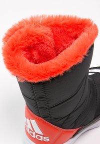 Czarny but z pomarańczowym sztucznym futrem, teksturowana tkanina i białe akcenty z logo Adidasa z boku.