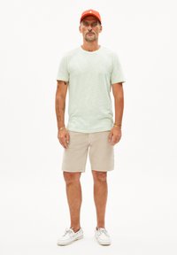 Lichtgroen T-shirt met korte mouwen, beige shorts en witte bootschoenen. Rode pet met logo. Soepele stof en casual pasvorm.