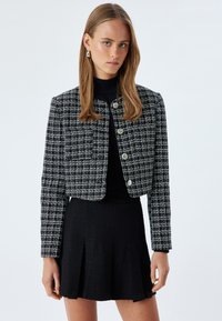Mustat ja valkoiset tweed-takit lyhyellä designilla, joissa on pyöreät hopeanväriset napit, yhdistettynä mustaan, teksturoituun hameeseen.