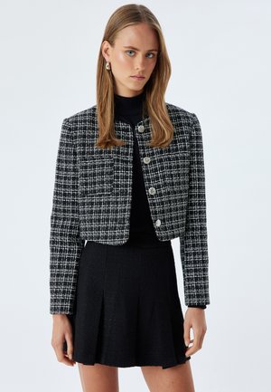 Zwart-witte tweedjas met een cropped ontwerp, voorzien van ronde zilveren knopen, gecombineerd met een zwarte textuur rok.