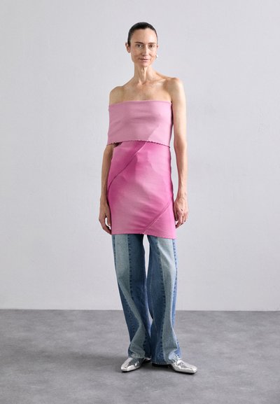 Zweiteiliges Outfit bestehend aus einem trägerlosen pinken Oberteil und einem pinken asymmetrischen Rock. Kombiniert mit hellblauen, ausgestellten Jeans und silbernen Schuhen.