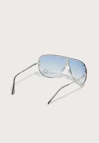 Sonnenbrille mit einem metallisch silbernen Rahmen, blauen Verlaufslinsen und sternförmigen Perforationen an der Seite. Elegantes Design im Pilotenstil.