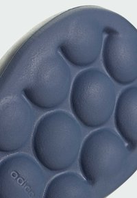 Ciemnoniebieska podeszwa buta z teksturowanym, bąbelkowym wzorem. Powierzchnia wydaje się gładka z zaokrąglonymi wklęśnięciami, co zapewnia wyściełany komfort. 