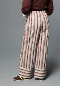 High waist, wijd uitlopende broek in een crèmekleur met verticale rood-zwarte strepen. Geverfd met een gerimpelde textuur; voorzien van omgeslagen zoom en zijzakken.