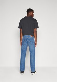 Schwarzes Kurzarm-T-Shirt kombiniert mit hellblauen Jeans. Die Jeans verfügen über zwei Gesäßtaschen und subtile Nähdetails. Schwarze Sneakers runden das Outfit ab.