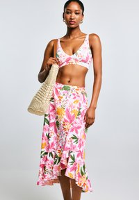 Ensemble floral deux pièces composé d'un crop top à motifs floraux roses et d'une jupe assortie avec un ourlet volanté, associé à un sac en paille.