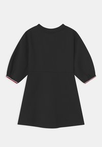 Czarna sukienka z teksturowanej tkaniny, z krótkimi bufkami i okrągłym dekoltem. Posiada czerwone i białe akcenty przy mankietach rękawów.
