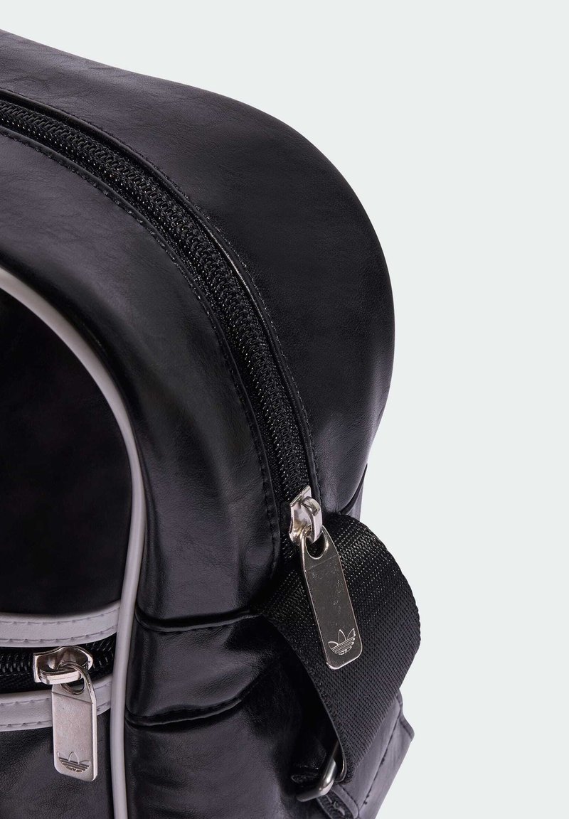 Black faux leather backpack corner with dual zippers, silver hardware, textured surface, and adjustable black strap detail.