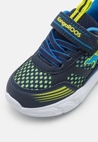 Sinine ja roheline võrgusneaker, millel on kollased detailid, mustriline disain, pehmendusega keelteosa, valge tald ja reguleeritav rihm.