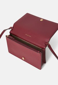 Rode leren handtas met een gestructureerde afwerking, gouden hardware en een ritscompartiment. Het interieur heeft een beige voering en logo-detail.