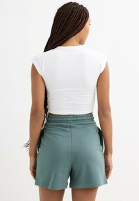 Top corto ajustado de manga corta en blanco, combinado con pantalones cortos de cintura elástica en color teal que cuentan con bolsillos laterales. Tejido suave con un ajuste cómodo.