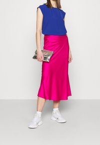 Modrý žebrovaný krátký rukáv top je kombinován s lesklou růžovou saténovou sukní ke kolenům. Kombinaci doplňuje stříbrná kabelka a bílé tenisky.