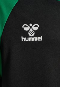 Schwarzes Sporttrikot mit grünen Akzenten an den Schultern und einem weißen Hummel-Logo auf der Brust, gefertigt aus strukturiertem Stoff.