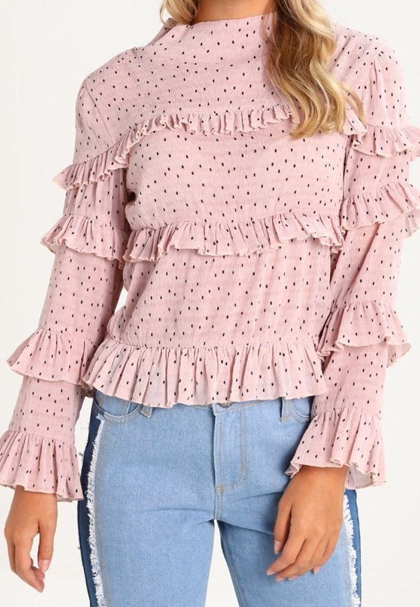 Světle růžová halenka s volánky a dlouhým rukávem s černými puntíky, s nařasenými detaily kolem výstřihu a rukávů, v kombinaci s džíny.