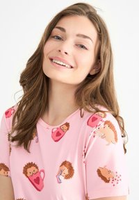 Ljusrosa t-shirt med rund halsringning och korta ärmar, med ett mönster av tecknade igelkottar och hjärt-temat grafik.