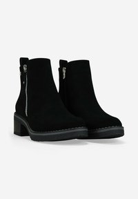 Botas de ante negras hasta el tobillo con tacones gruesos y cremalleras laterales, diseñadas para uso casual o formal.