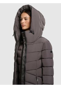 Chaqueta de abrigo gris con una gran capucha, con diseño acolchado, cierre frontal de cremallera y bolsillos laterales. Textura suave y lisa con acentos mínimos.