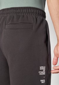 Pantalon de jogging noir avec ceinture élastique, doté d'une poche arrière et d'un imprimé en blanc indiquant "WORLD SERIES OF FITNESS RACING SINCE 2017."