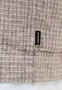 Beige og brunt teksturert vevd stoff med en liten svart vevd etikett sydd på med teksten "JACK & JONES".