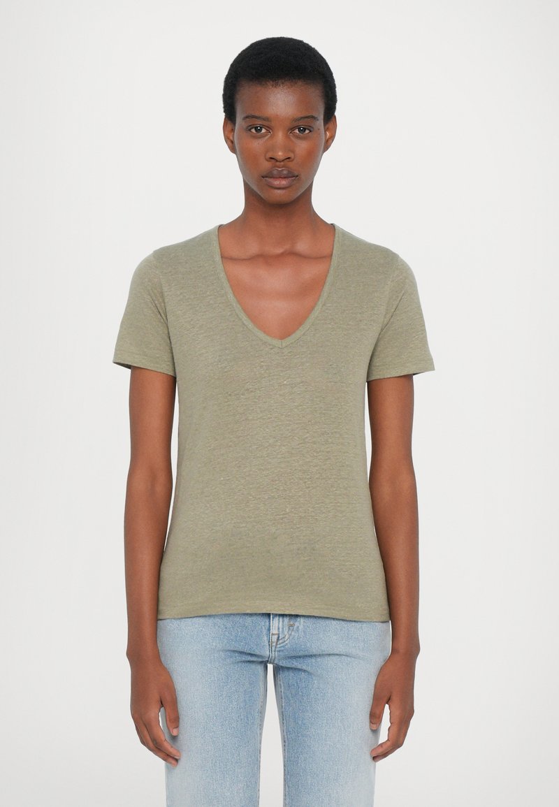 Olivgrön V-ringad t-shirt gjord av mjukt, texturerat tyg med korta ärmar. Buren med ljusblå åtsittande jeans, framifrån.