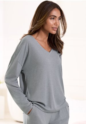 Gray, ribbed long-sleeve top with a V-neckline and relaxed fit. Soft texture, worn with hands in pockets, paired with matching pants.