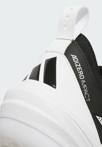Black and white athletic shoe with a textured upper, prominent logo, and reflective accents. Features a sturdy heel and pull tab.
