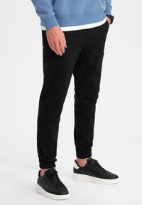 Svarta joggerbyxor med en åtsittande passform, elastiska manschetter och sidofickor. Matchas med stiliga svarta sneakers med en vit sula.
