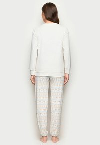 Hvid langærmet top med rund halsudskæring kombineret med mønstrede pyjamasbukser med lyseblå og orange motiver af cocktails og snefnug.