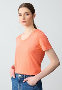 T-shirt a maniche corte in tessuto corallo, con scollatura rotonda e trama liscia. Abbinato a jeans in denim blu a vita alta.