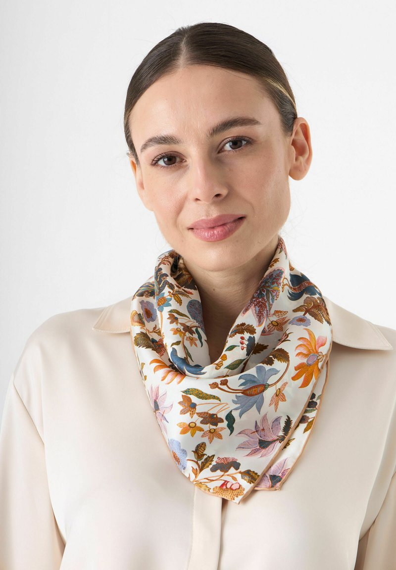 Foulard en soie avec un motif floral en bleu, orange et rose sur un fond crème, porté en boucle autour du cou.