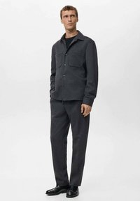 Camicia grigia con bottoni e due tasche sul petto, abbinata a pantaloni grigi coordinati e scarpe nere. Tessuto liscio, design semplice e moderno.